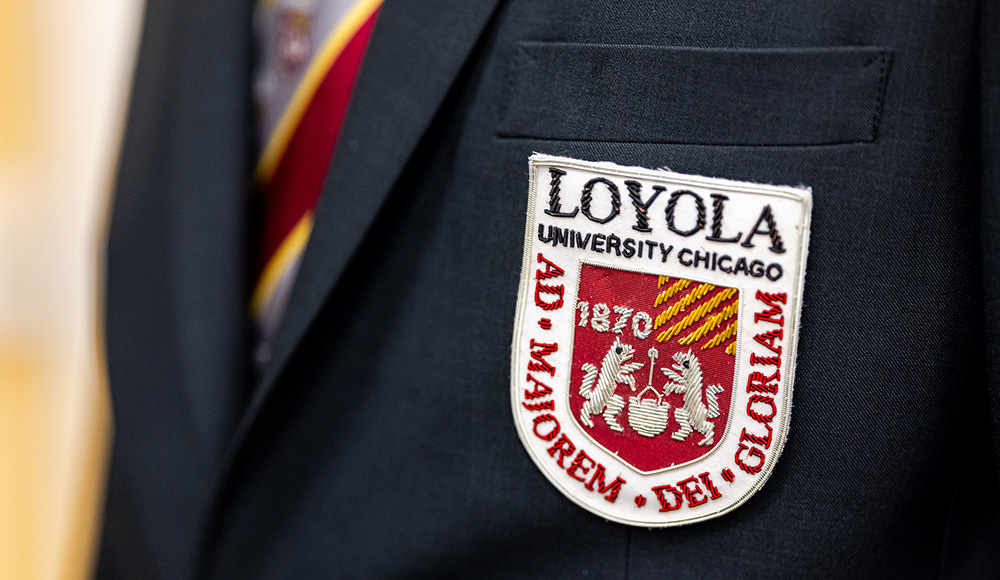 A closeup of a man wearing a sportcoat with an embroidered patch of Loyola's logo on the breast. A closeup of a man wearing a sportcoat with an embroidered patch of Loyola's logo on the breast.