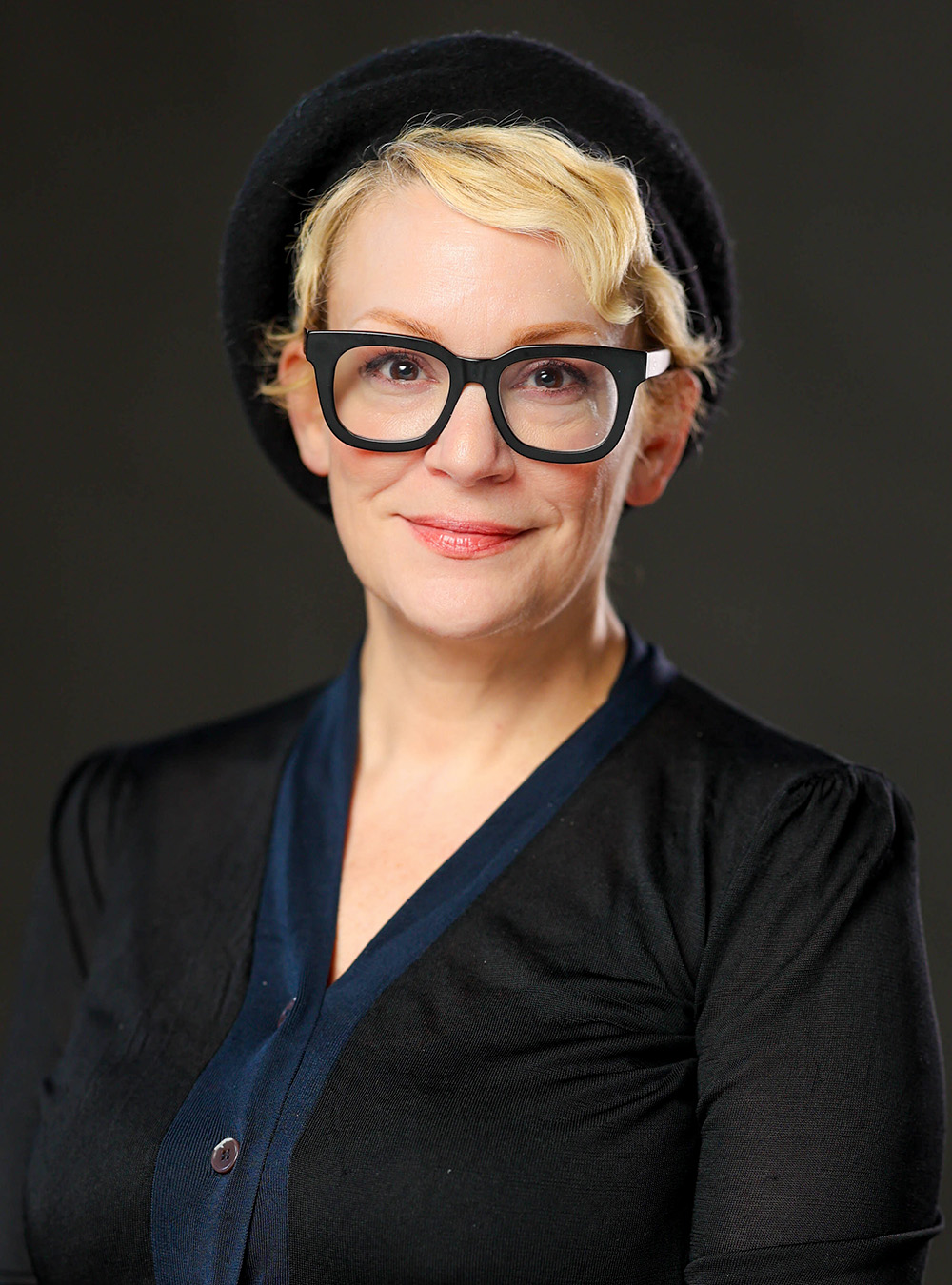 Portrait of a smiling woman with short blonde hair wearing a black beret and black top against a dark background× Portrait of a smiling woman with short blonde hair wearing a black beret and black top against a dark background×
