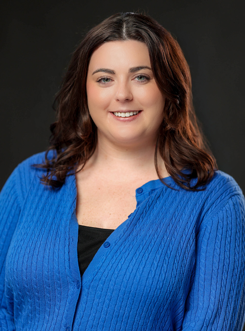 Portrait of a woman with long dark hair wearing a blue sweater against a dark background Portrait of a woman with long dark hair wearing a blue sweater against a dark background