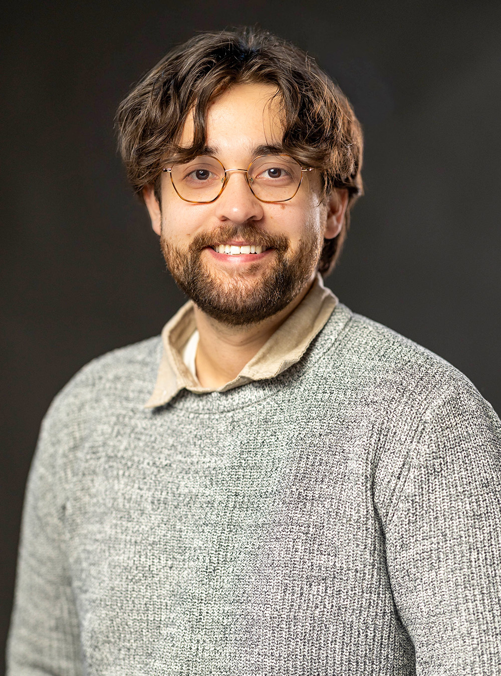 Portrait of a smiling man with glasses and a beard wearing a light sweater against a dark background Portrait of a smiling man with glasses and a beard wearing a light sweater against a dark background
