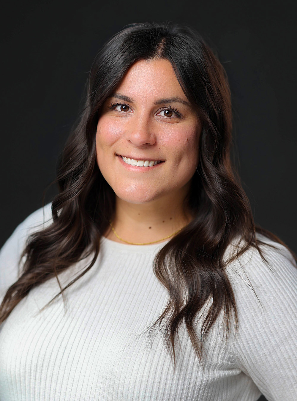 Portrait of a woman with long dark hair wearing a beige sweater against a dark background Portrait of a woman with long dark hair wearing a beige sweater against a dark background
