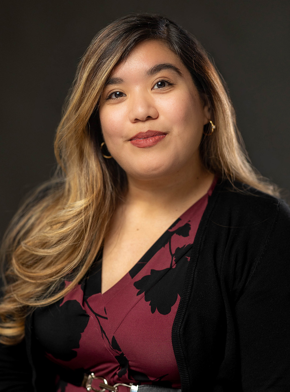 Portrait of a woman with long highlighted hair wearing a patterned dress and black cardigan against a dark background Portrait of a woman with long highlighted hair wearing a patterned dress and black cardigan against a dark background