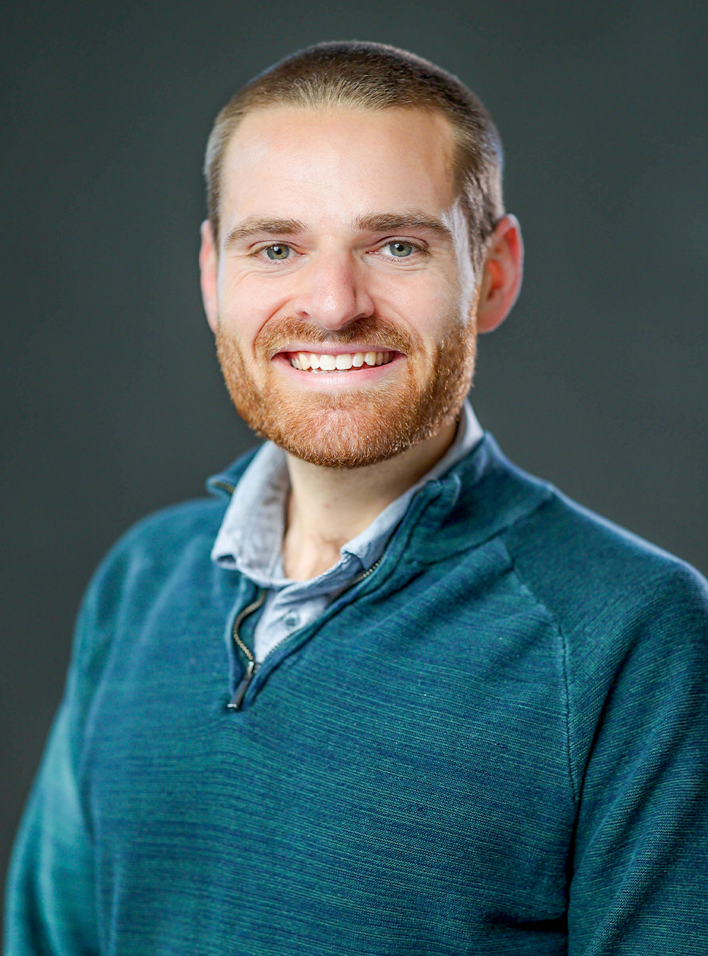 Portrait of a smiling man with short hair and a red beard wearing a green sweater against a neutral background Portrait of a smiling man with short hair and a red beard wearing a green sweater against a neutral background