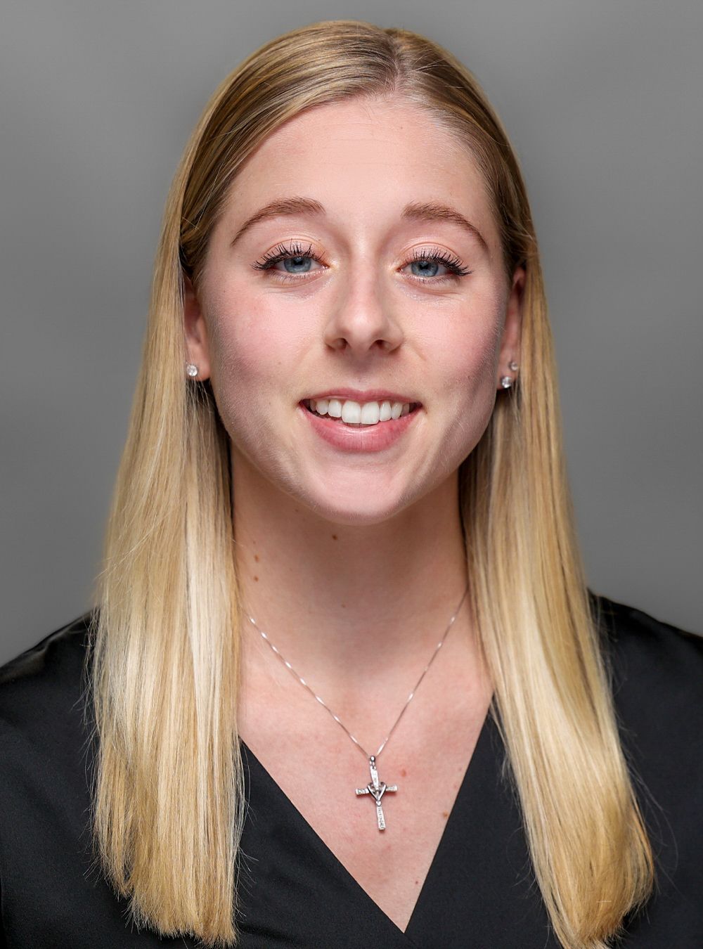 Portrait of a smiling woman with long blonde hair wearing a black top against a dark background