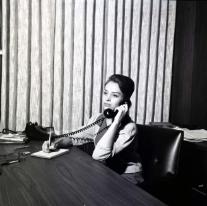 A woman holds a telephone receiver to her ear as she listens to a caller.