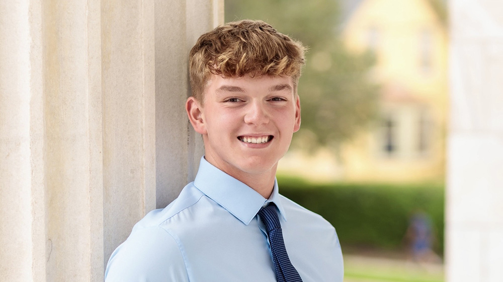 Portrait of a smiling student in business attire standing beside stone columns on Loyola University Chicago’s campus.