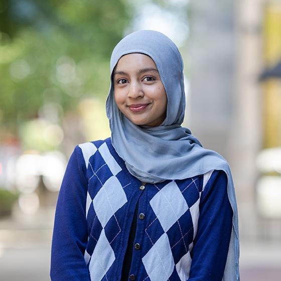 Portrait of a smiling student wearing a light blue hijab and blue argyle sweater on Loyola University Chicago’s campus.