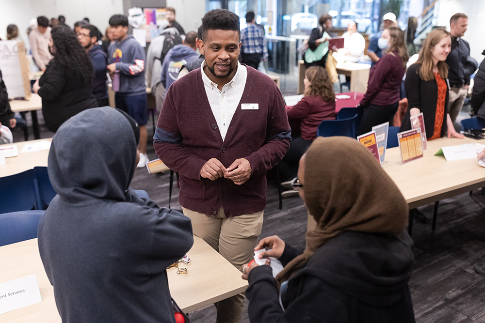 Staff member talking with students at a table during a resource fair.