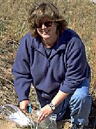 professor wearing a blue sweater kneeling in a grassing field