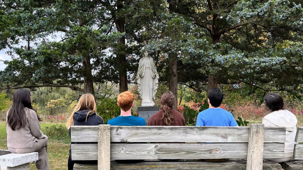 the back of six students heads facing a Mary statue outdoors the back of six students heads facing a Mary statue outdoors