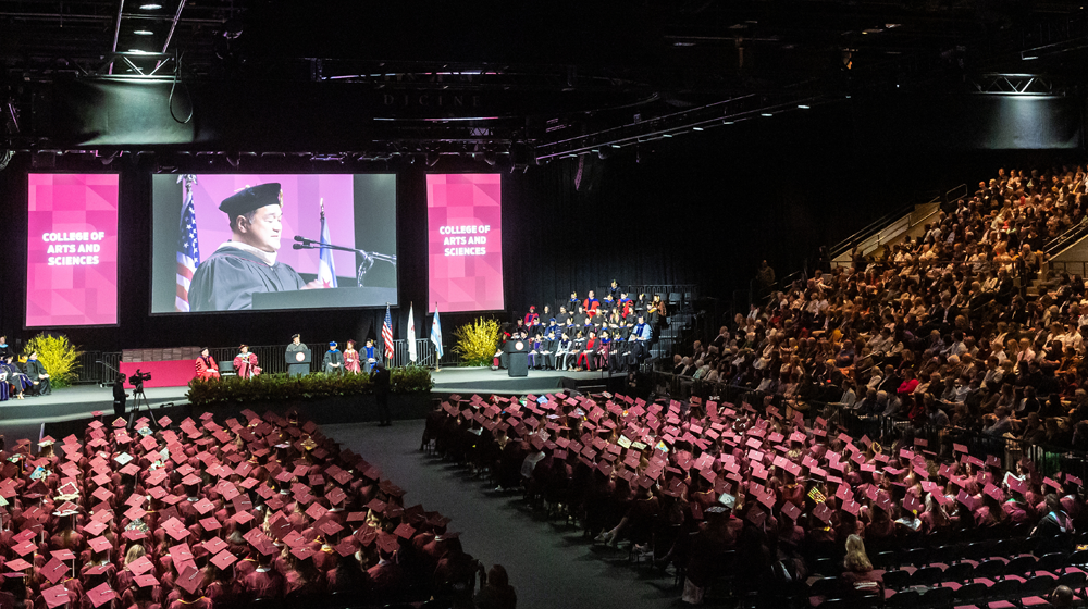Large crowd in arena listening to commencement speaker on screen 