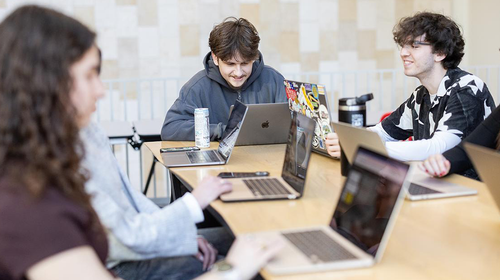 Students sitting at a table with computers open 