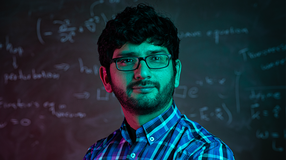 Walter Tangarife, Assistant Professor of Physics, in front of a chalkboard with equations on it