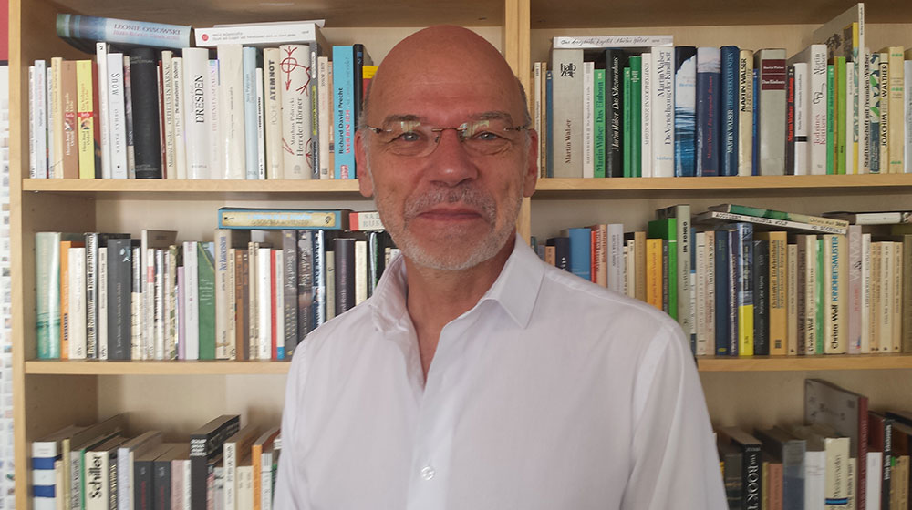 Reinhard Andress smiling in the foreground with bookshelves in the background