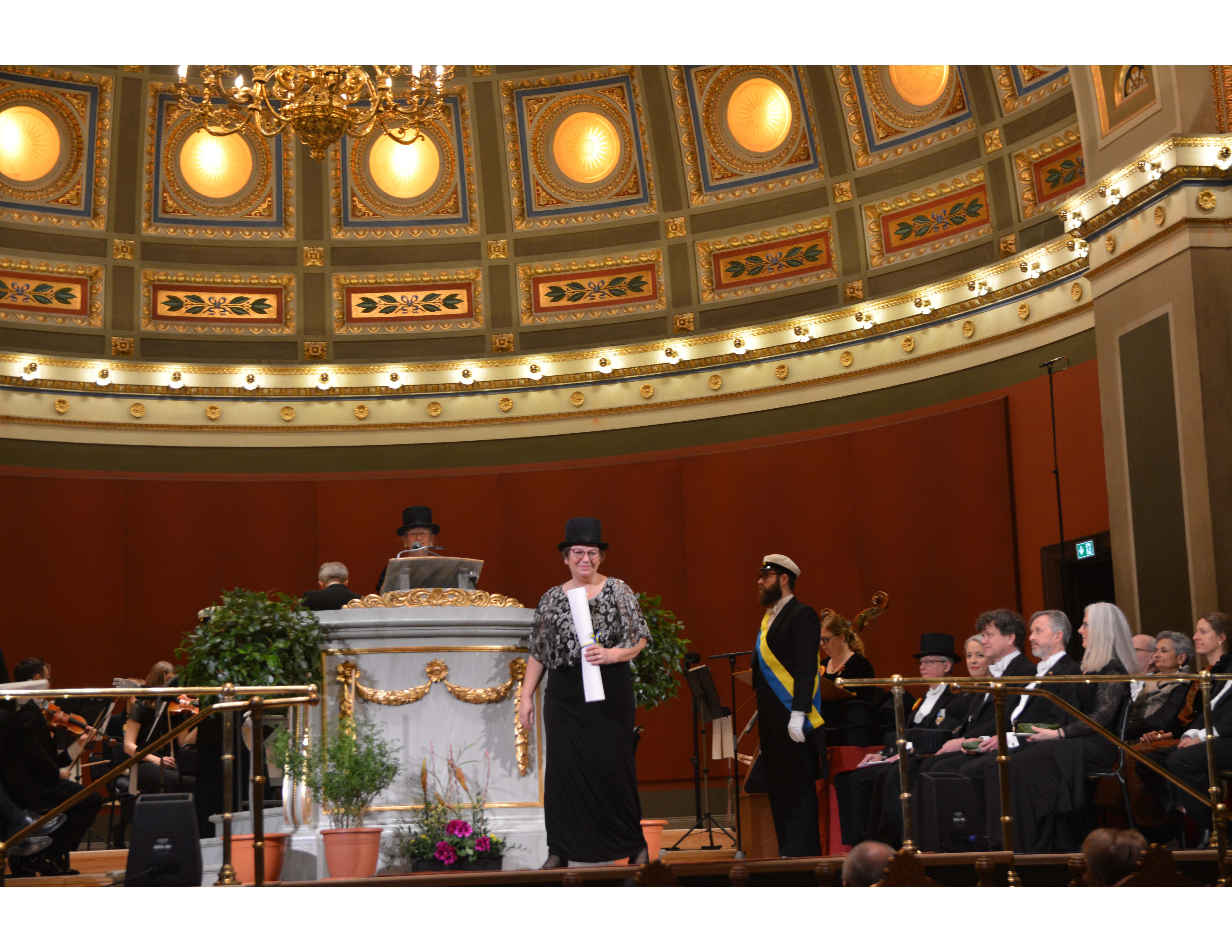 Hille Haker accepts her honorary doctoral degree, hat, and ring on stage at the ceremony at Uppsala University