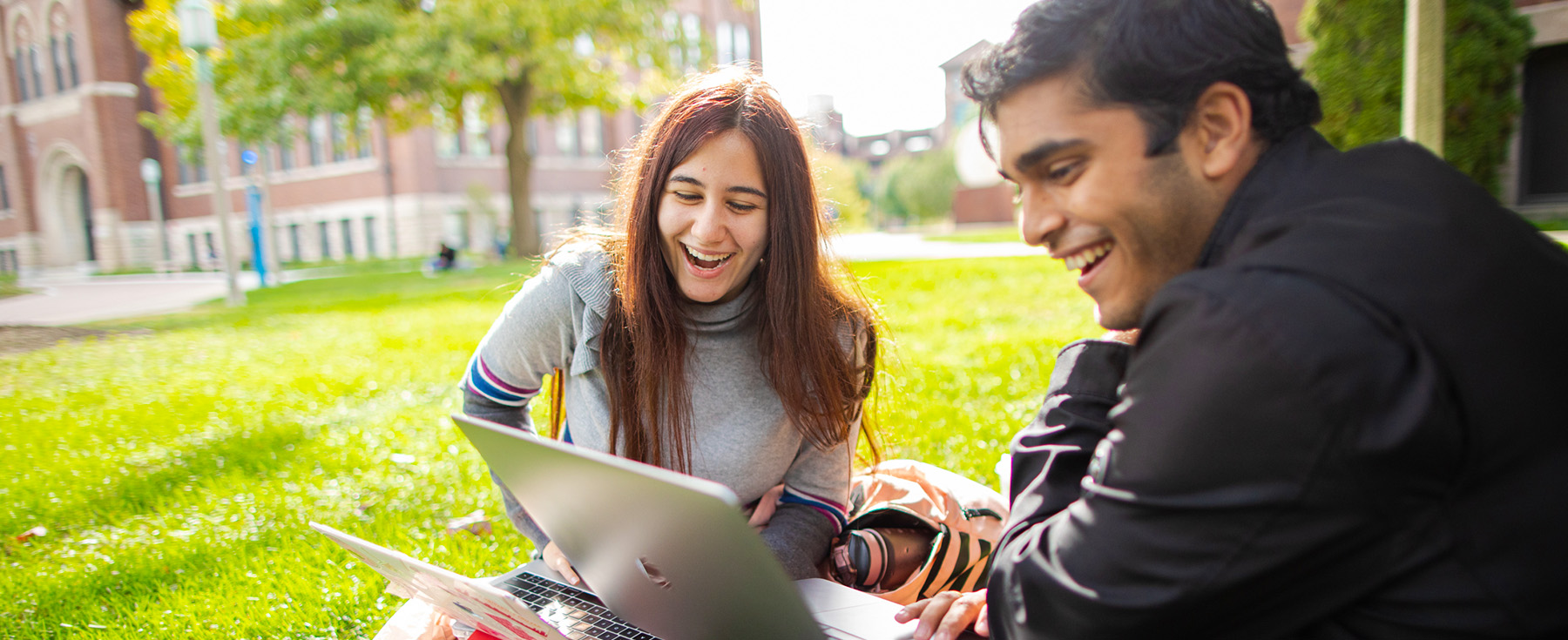 Students looking at a laptop sitting outside in the sun Students looking at a laptop sitting outside in the sun