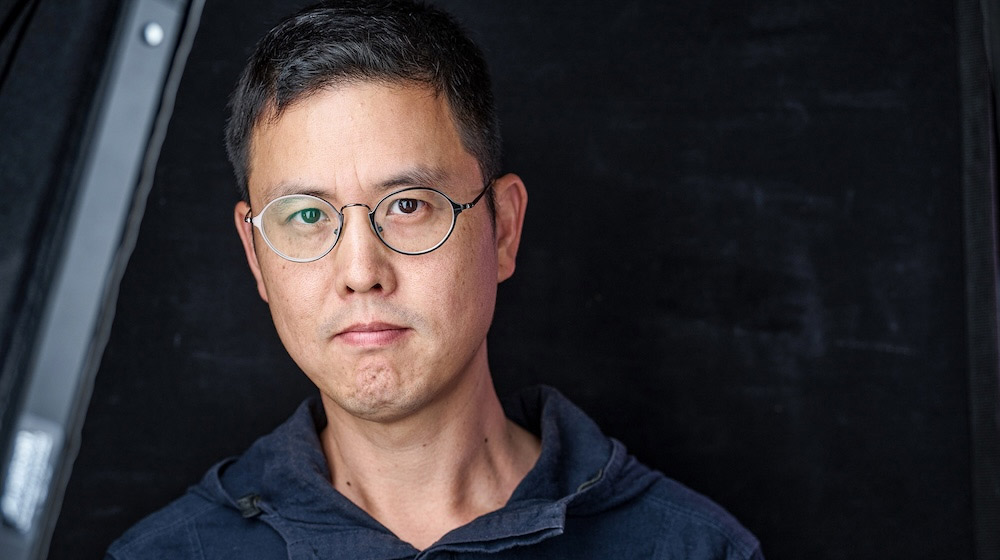 Man's face with glasses looks at camera in dark room