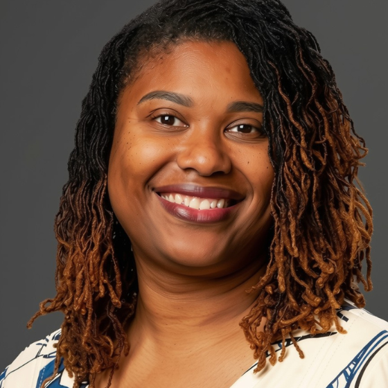 A woman with medium long brown hair in twists, smiling and wearing a white-ish top, against a solid grey background. A woman with medium long brown hair in twists, smiling and wearing a white-ish top, against a solid grey background.