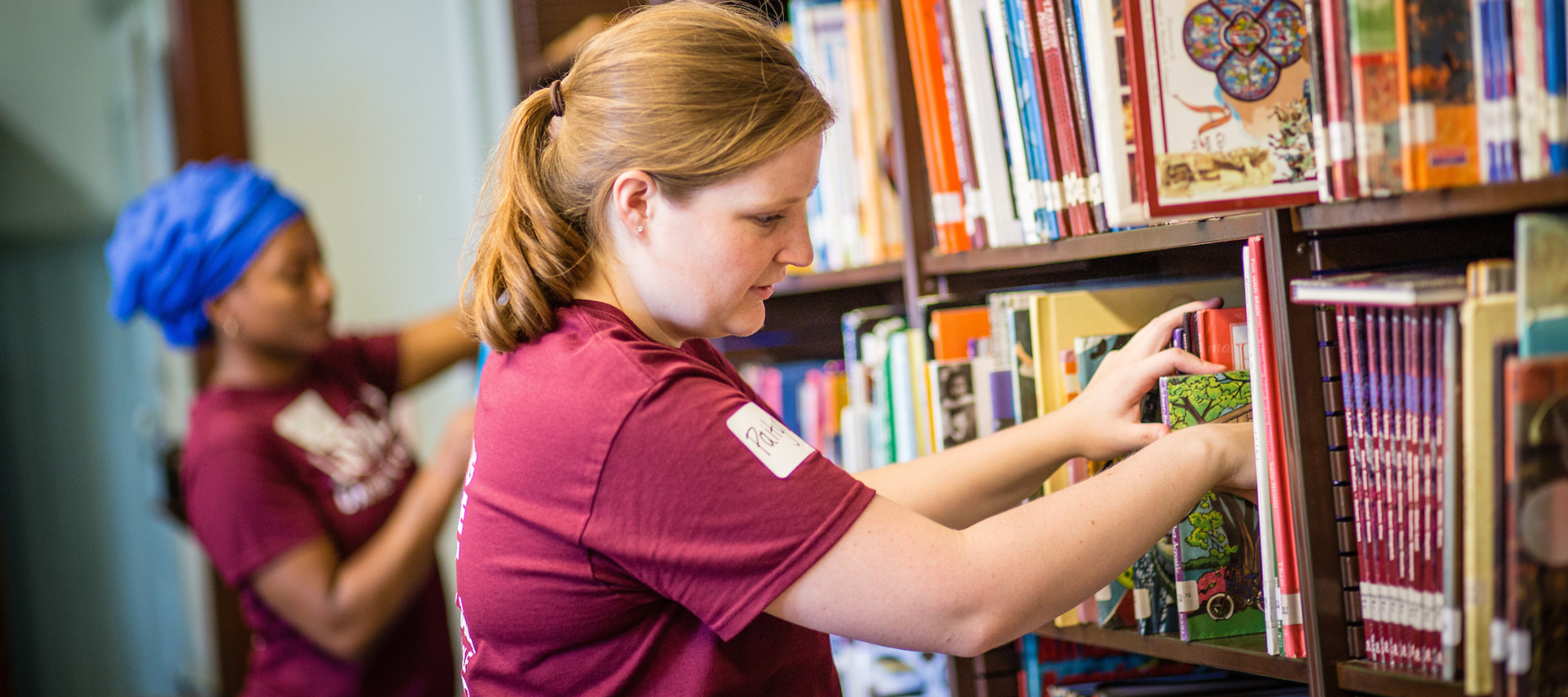 student teacher volunteering in a school library organizing books. 