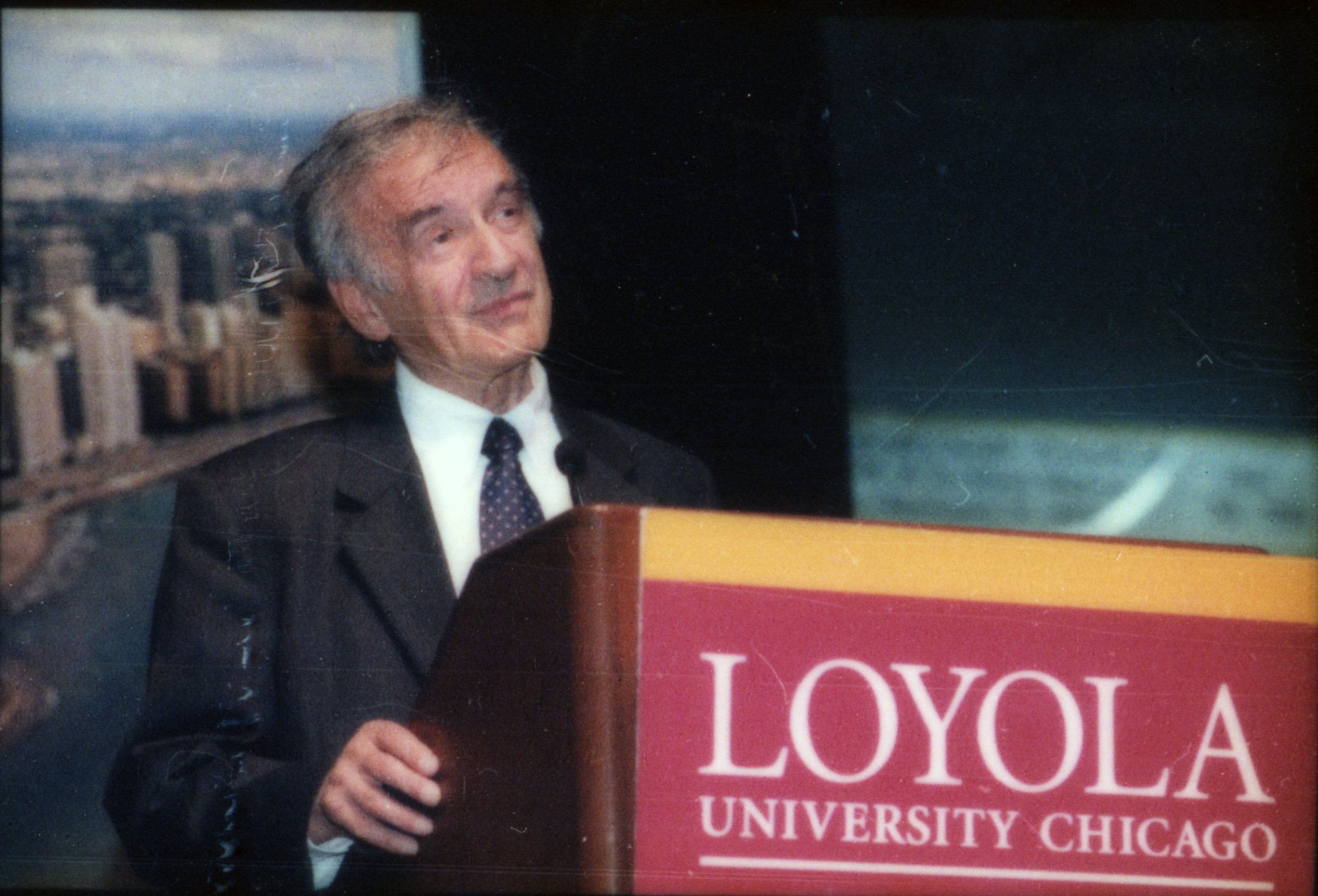 An older man in a suit and tie speaking at a podium at Loyola