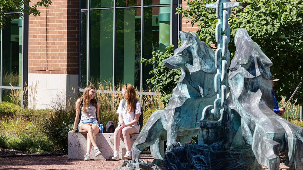 Two students sit on a bench near the Los Lobos, or Two students sit on a bench near the Los Lobos, or