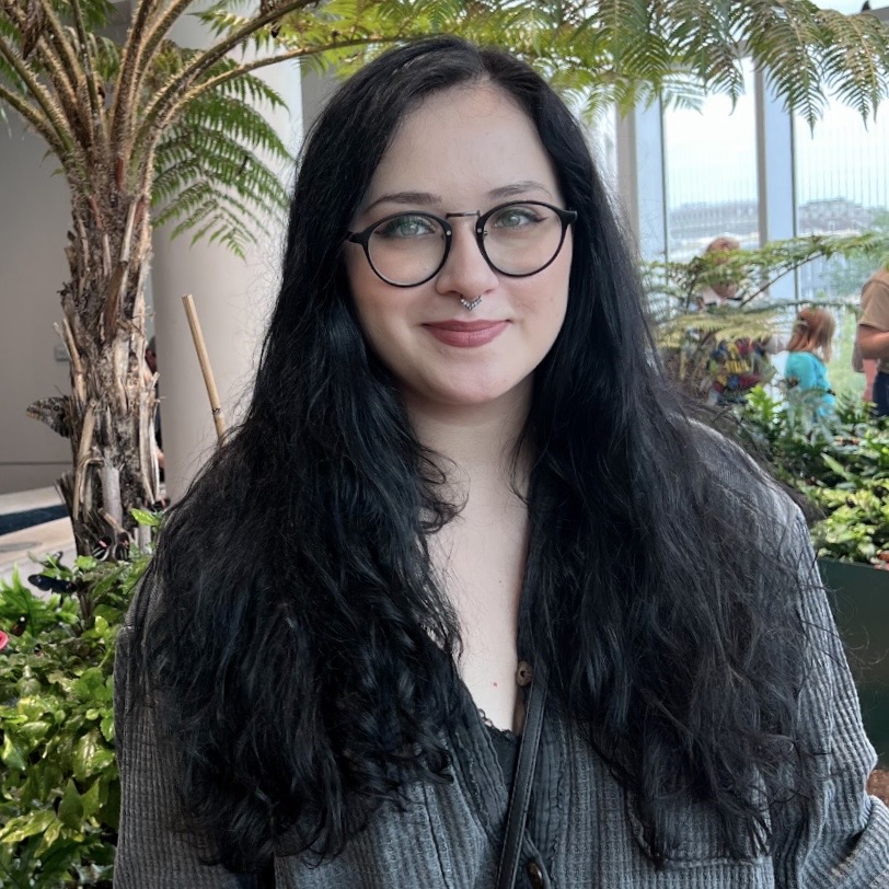 dark haired woman with glasses poses in front of plants dark haired woman with glasses poses in front of plants