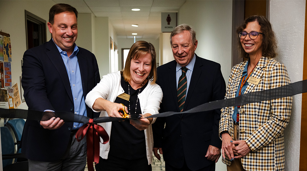 Four people participate in a ribbon cutting ceremony inside a hallway