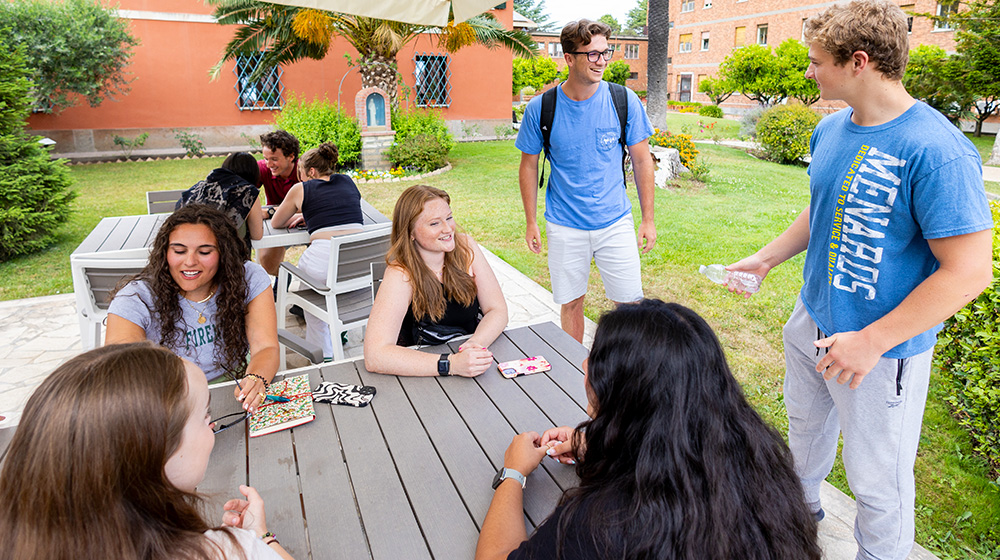A group of JFRC students converse outdoors at a campus plaza