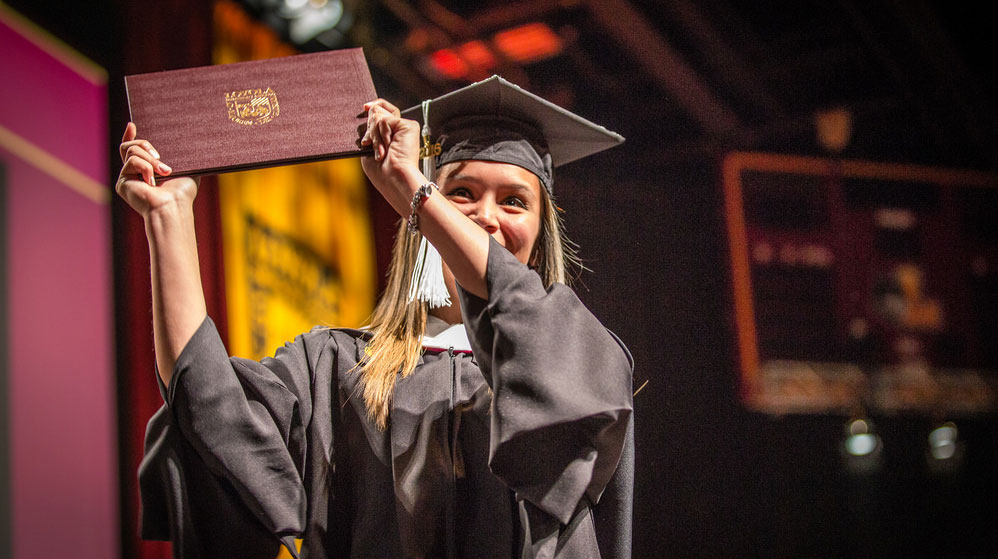 A woman in a graduation gown proudly holds her diploma, symbolizing her academic achievement and success. A woman in a graduation gown proudly holds her diploma, symbolizing her academic achievement and success.