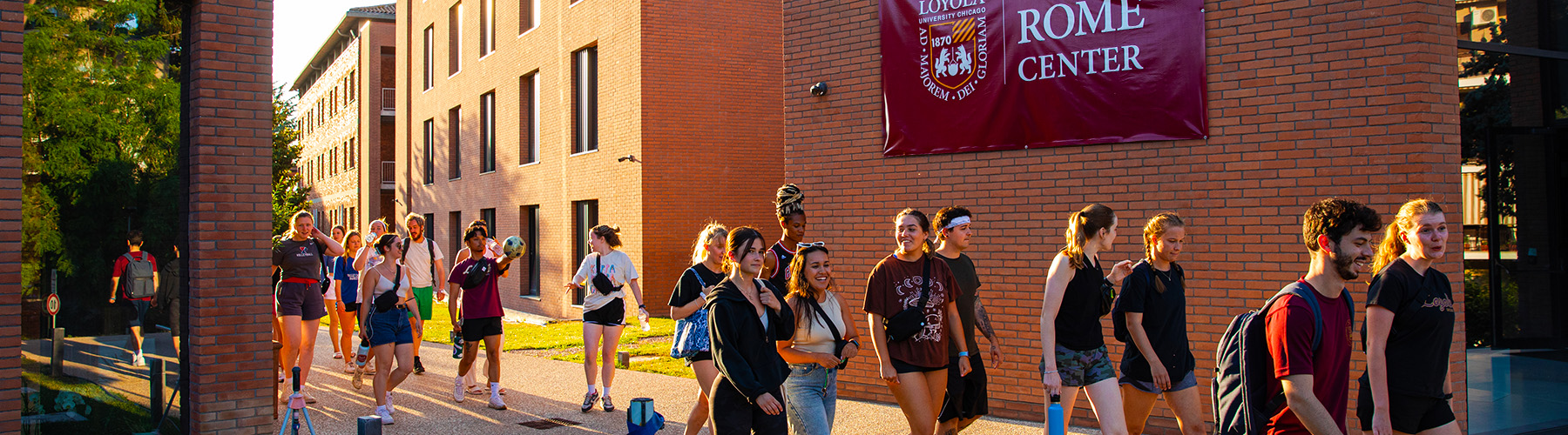 A large group of students walk along the outside of the Rome Center