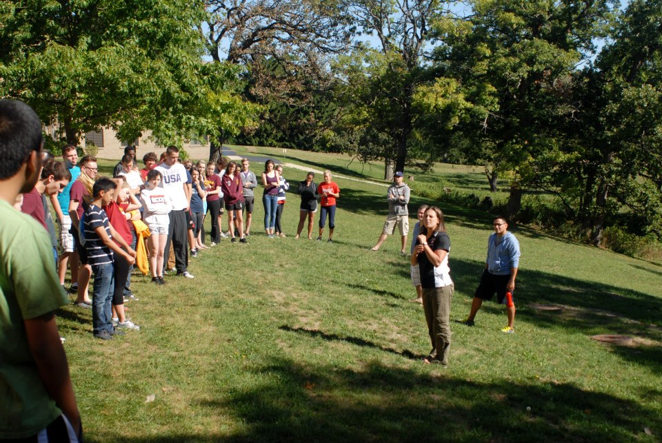 A large group of people gather in a clearing for a structured retreat