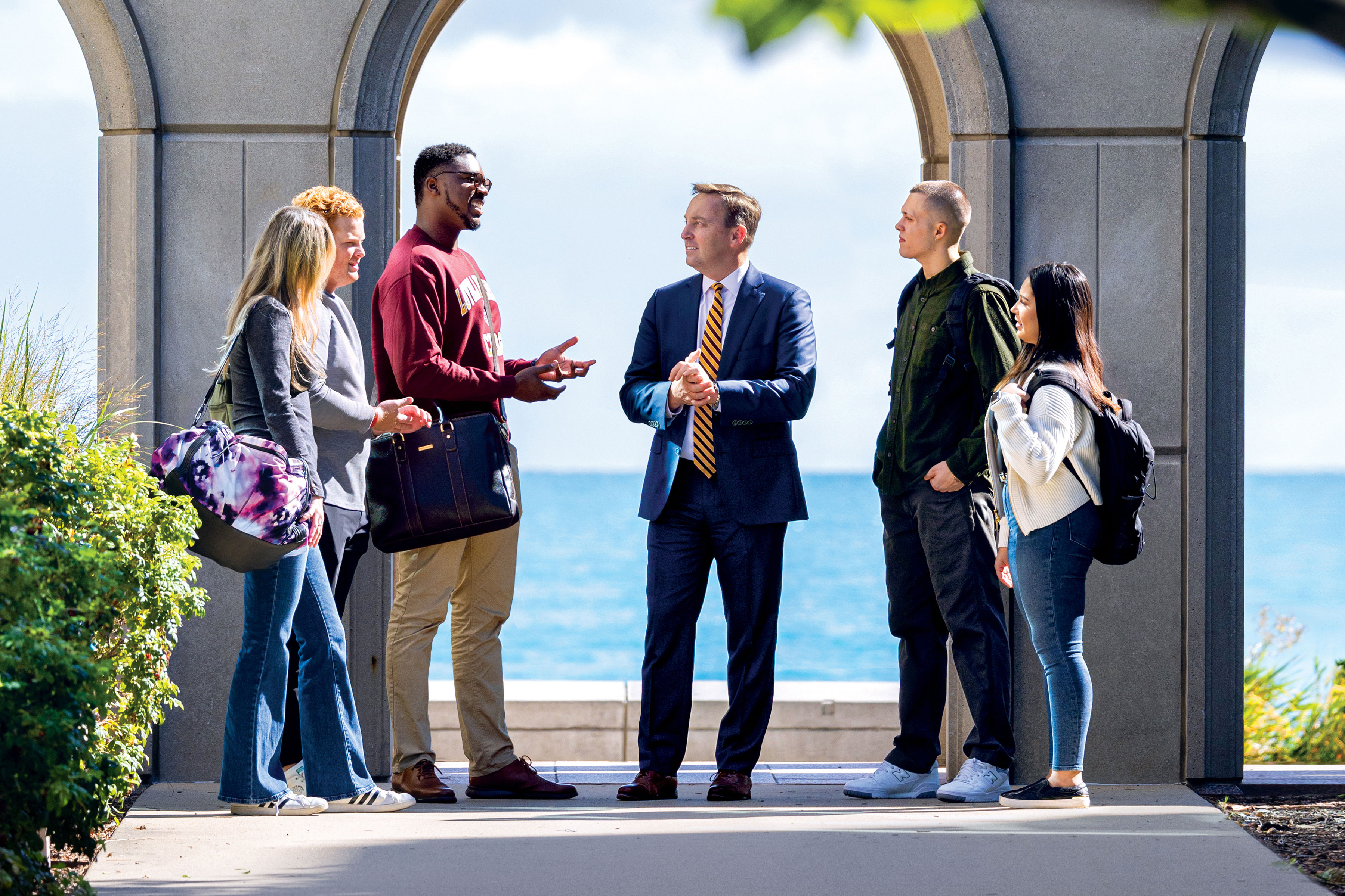 Loyola president Mark C. Reed talks with five students in front of Lake Michigan