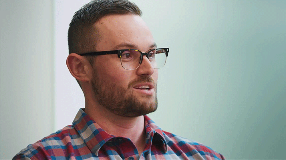 Side profile headshot of a man with short brown hair and glasses, wearing a plaid shirt