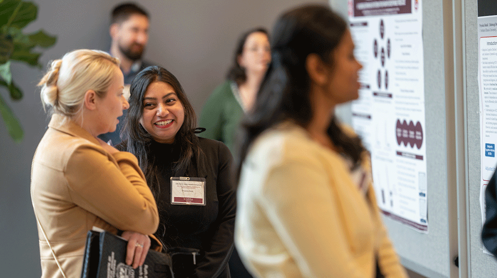 People smile and talk while looking at research posters People smile and talk while looking at research posters