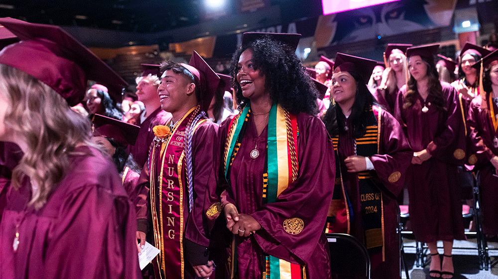 Loyola Nursing graduates in commencement gowns stand and smile during the commencement ceremony