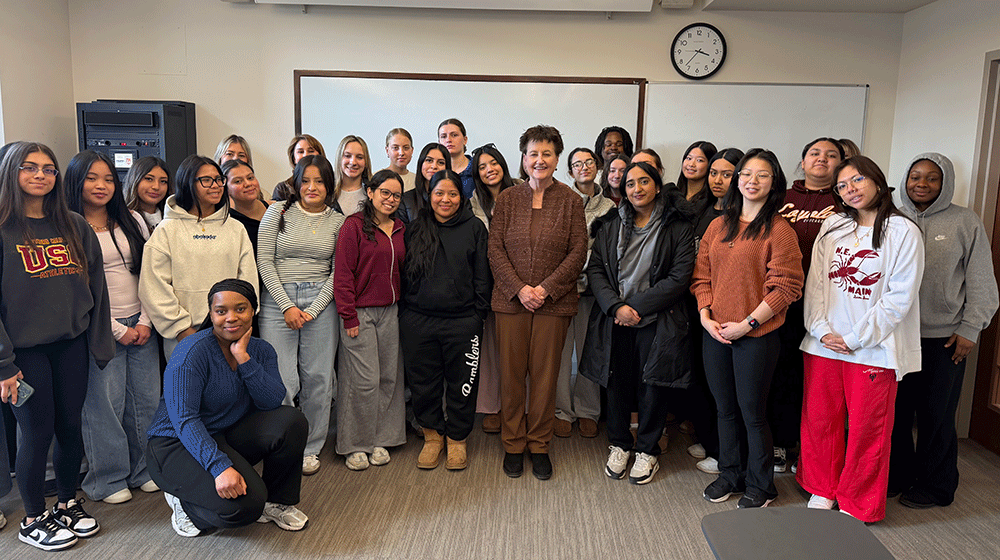 The dean stands in front of a white board in a classroom with college students, mostly female, beside her The dean stands in front of a white board in a classroom with college students, mostly female, beside her