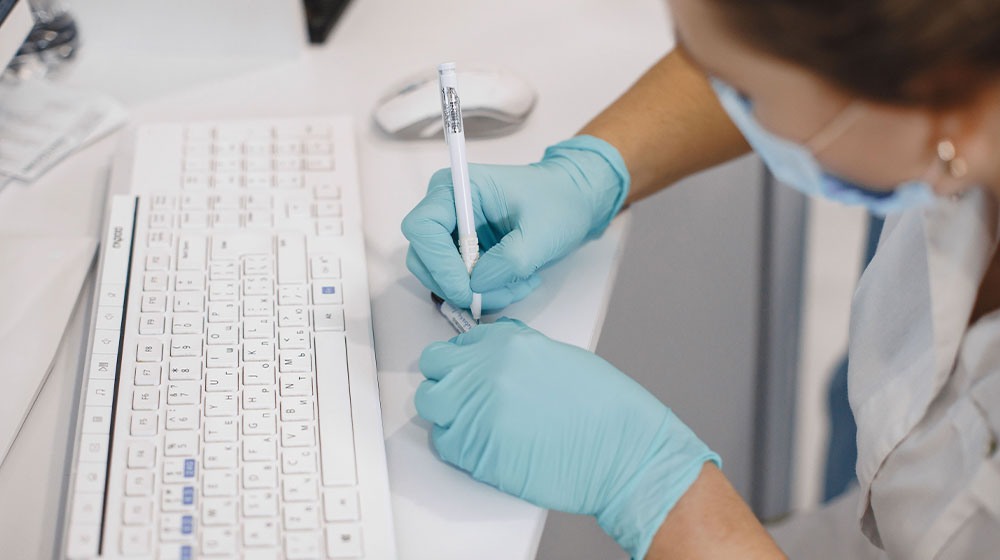 Close up of a masked nurse writing on a test tube