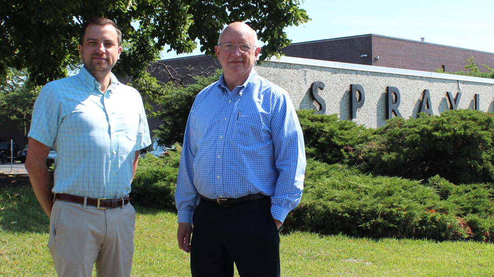 Two men in business attire pose for a photo in front of a commercial landscape. Two men in business attire pose for a photo in front of a commercial landscape.