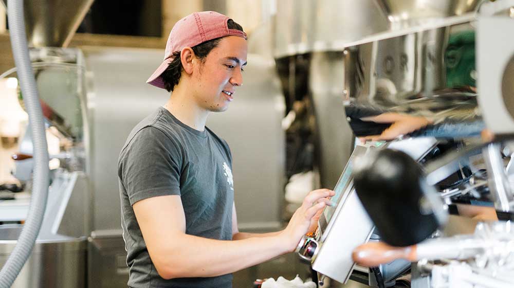 Image of Harry Hutchins next to his coffee roaster Image of Harry Hutchins next to his coffee roaster
