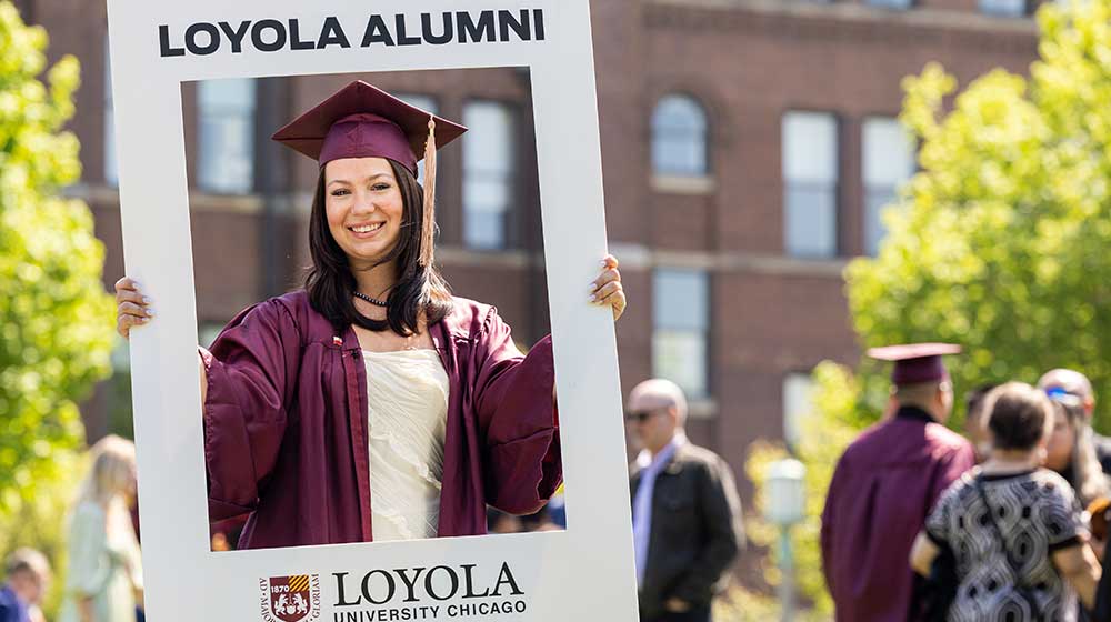 Student in graduation cap and gown holding a sign saying 