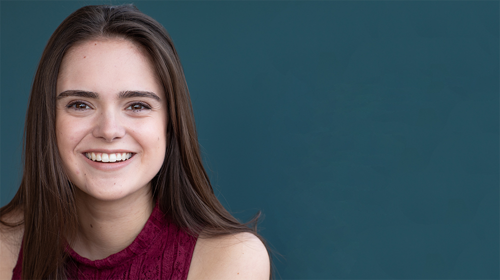 Female student smiling against a turquoise background.