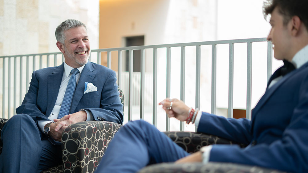 Eric Holler in a blue suit sitting with a student inside the Schreiber Center.