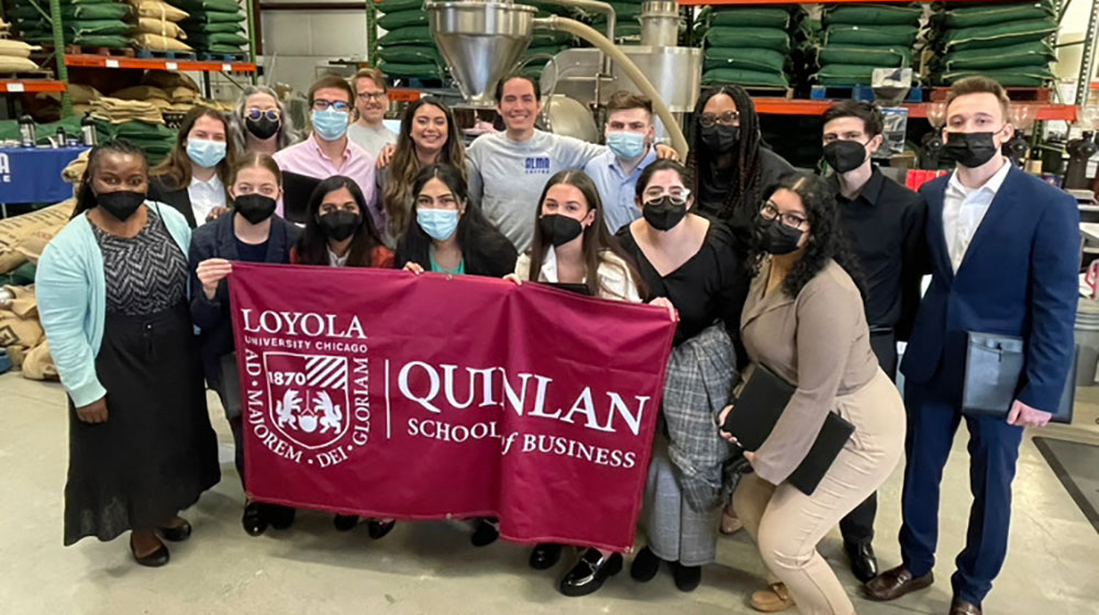 A group of students in a factory holding a Quinlan banner A group of students in a factory holding a Quinlan banner