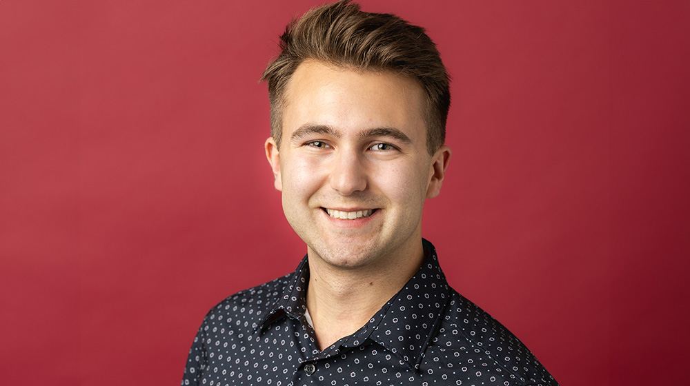 Headshot of Jason Janiga in blue shirt against a red background