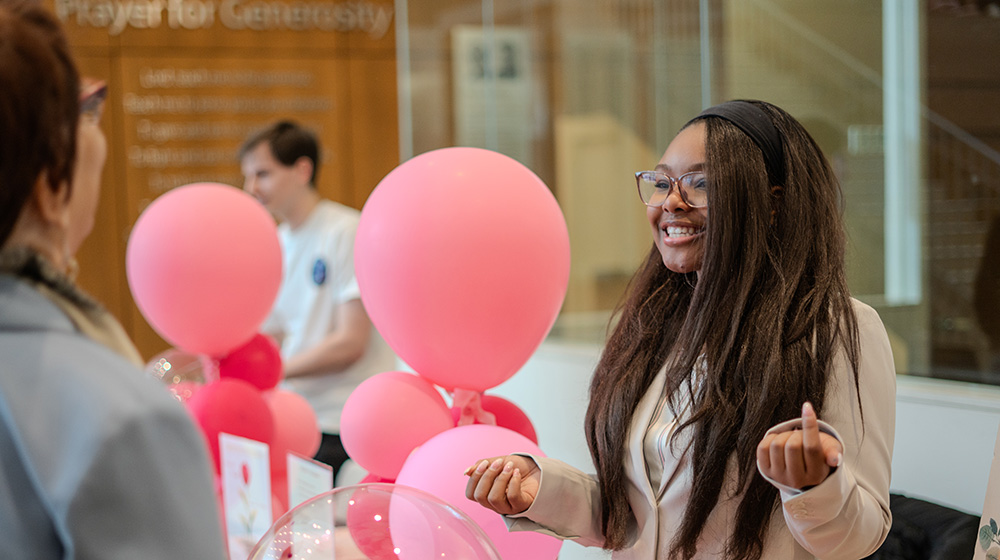 A quinlan student smiles in front of pink balloons from her business poster