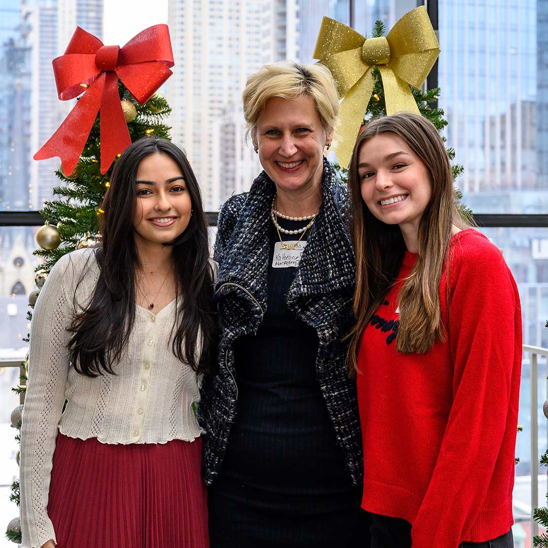 A professor and two students in front of Christmas trees and the Chicago skyline