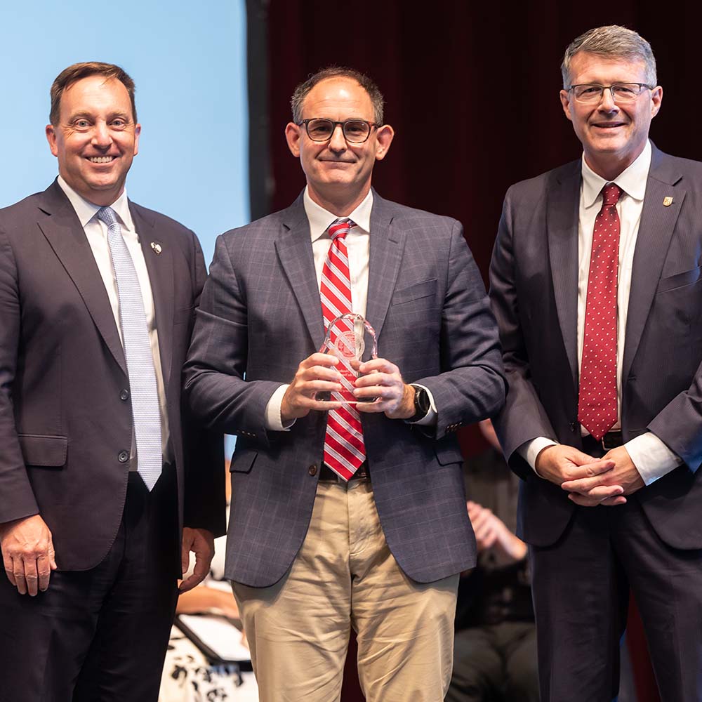 Mike Hewitt stands with President Mark Reed (left) and Provost Doug Woods (right)..