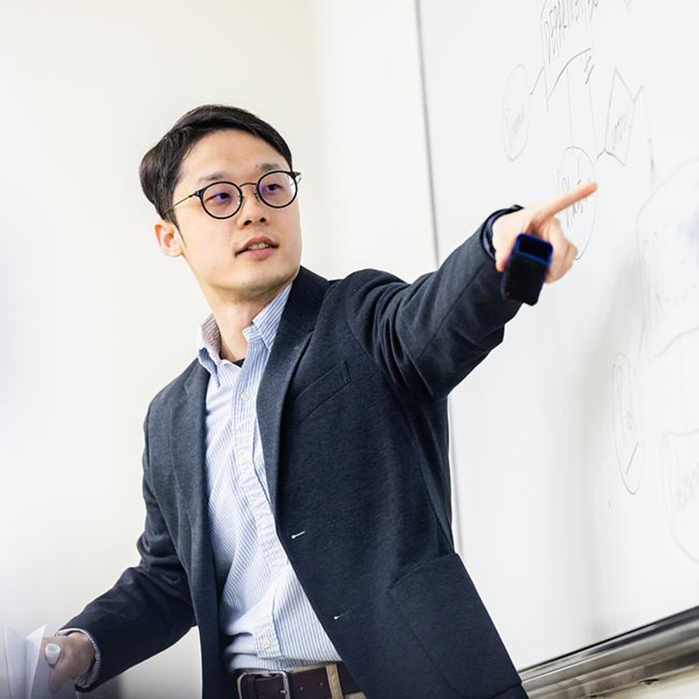 Yuxiao Rain Luo stands and points at writing on a whiteboard