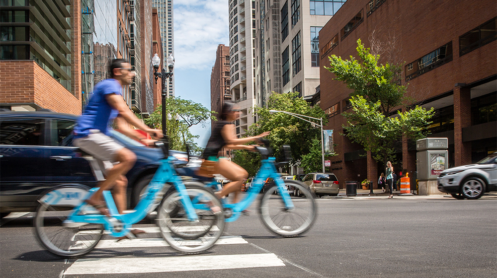 Two individuals ride bikes downtown near the Water Tower Campus. 