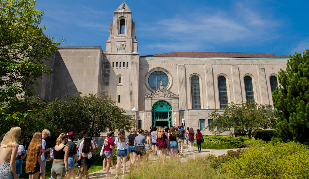 A group of people walking in front of a large building with a clock tower.
